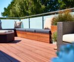 Entspannte Terrasse mit Holzdecks, Sitzkissen und Blick auf grüne Bäume im Hintergrund.