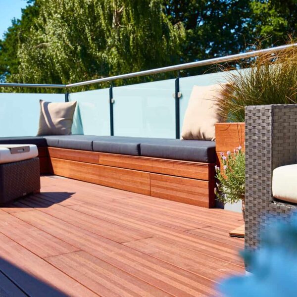 Entspannte Terrasse mit Holzdecks, Sitzkissen und Blick auf grüne Bäume im Hintergrund.