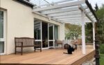 Terrasse mit Pergola, Gartenmöbeln und Katze im Außenbereich.