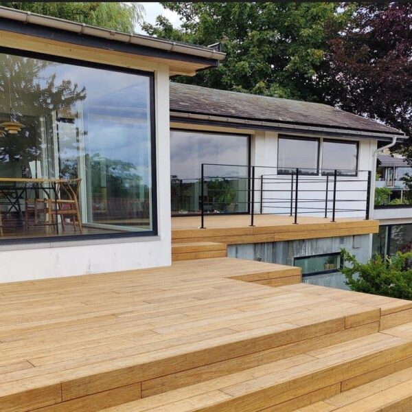 Moderne Holzterrasse vor einem Haus mit Glasfront und Blick ins Grüne.
